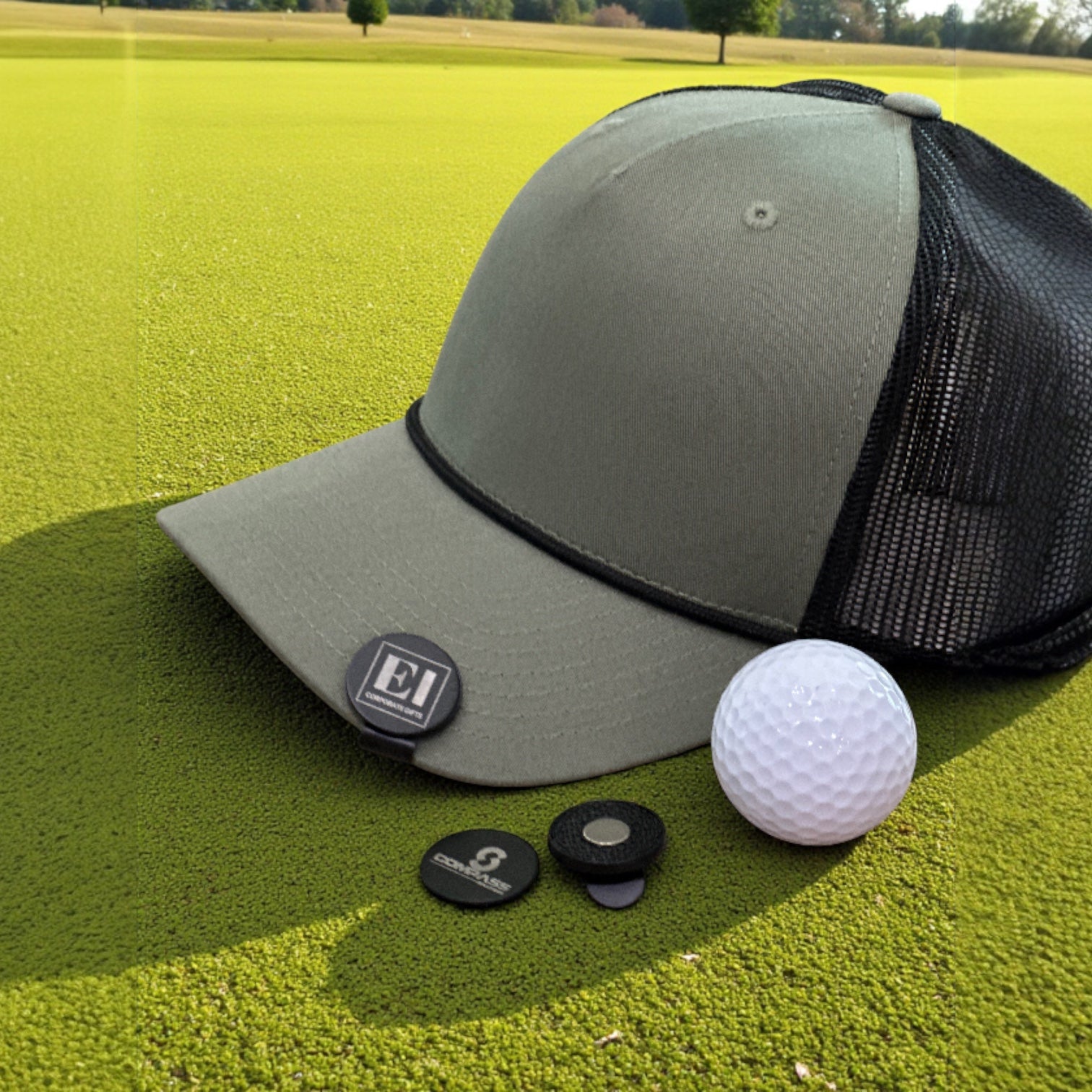 A custom laser engraved magnetic golf marker hat clip sitting on green grass next to a golf ball. Perfect for businesses, corporations, and golf tournaments. Personalized with your logo or design, this stylish and functional golf accessory makes a professional gift for clients, employees, or tournament participants.