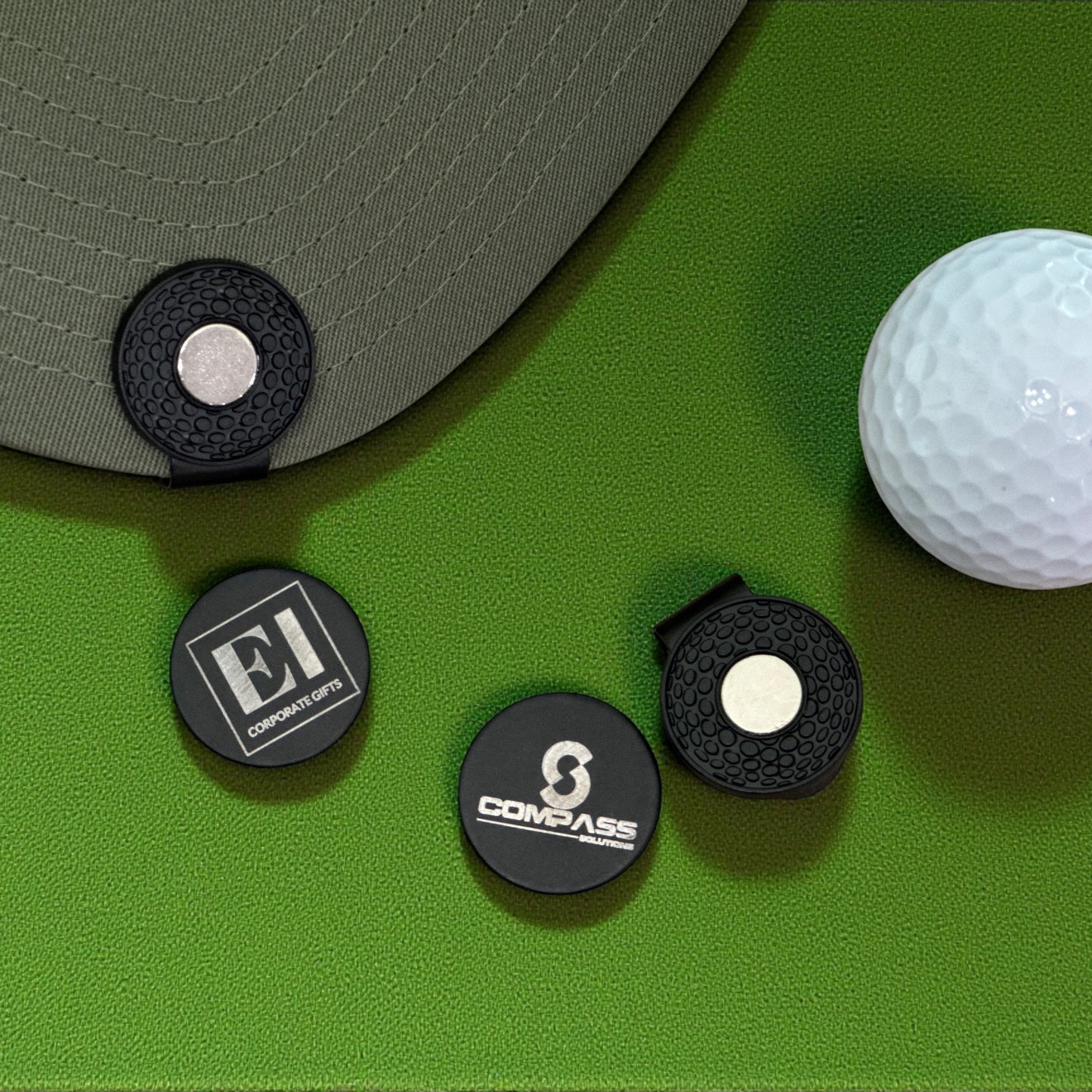 A custom laser engraved magnetic golf marker hat clip sitting on green grass next to a golf ball. Perfect for businesses, corporations, and golf tournaments. Personalized with your logo or design, this stylish and functional golf accessory makes a professional gift for clients, employees, or tournament participants.